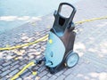 Street electric pressure washer stands on paving slabs among dry leaves and sunlight