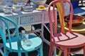 Street Fail Garage Sale Vintage Antique Dishes on Wicker Desk next to Colorful Wooden Brightly Painted Chairs