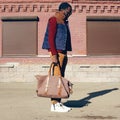 Street fashion look concept stylish african young man wearing vest jacket, sweater, bag walking in city evening, vintage colors Royalty Free Stock Photo