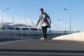 Street fashion and urban lifestyle: hipster man in trendy casual clothes on longboard on city road