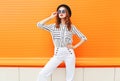 Street fashion woman model wearing a black hat sunglasses white pants over colorful orange Royalty Free Stock Photo