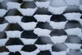 Street fence of thin mesh hawser with snowflakes accumulated in cells and half filled holes