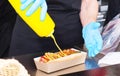Street food cart worker prepares a hot dog. Gloved hands add mustard to the hot dog