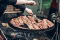 street food festival. grilled ribs meat. man holding steel tongues and roasting beef pork on big grill. chef in black form