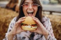 Street food festival. Stylish hipster girl in sunglasses eating delicious vegan burger at street food festival. Happy boho woman
