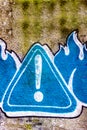 Street graffiti in the shape of a blue triangle and an exclamation mark inside. Road sign ATTENTION