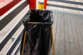 Street iron trash can with a black garbage bag on a wooden deck
