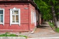 A street of Kaluga, Russia: an old red wooden house with white window frames, fresh green trees and couple in the distance