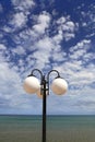 Street lamp against the blue sky with white clouds and sea Royalty Free Stock Photo