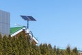 Street lamp with a solar panel behind green trees against a background of roofs and blue sky Royalty Free Stock Photo