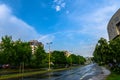 Street with lampposts and trees after the rain under the sky with rainbow