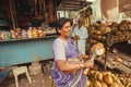 Street life and woman cutting coconut for milk near rustic store with food and snacks