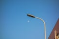 Street light against the clear blue sky, the full moon is visible in the daylight Royalty Free Stock Photo
