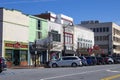 A street lined with lined with shops, restaurants, office buildings and bars with parked cars with a gorgeous blue sky