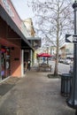 A street lined with shops and restaurants with tall black light posts and cars on the street and people on the sidewalk