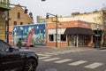 A street lined with shops and restaurants with tall black light posts and cars on the street and people on the sidewalk