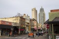 A street lined with shops and restaurants with tall black light posts and cars on the street and people on the sidewalk