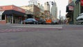 A street lined with shops and restaurants with tall black light posts and cars on the street and people on the sidewalk