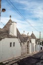 A street with lots of typical white houses in alberobello with nice pointed roofs with blue skies