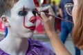 Street makeup for halloween. The make-up artist paints the guy`s face like a clown Pennywise. A teenager in an IT costume on a