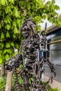 Street metal sculpture of a robot with machine gun made of old cars parts and details, auto-waste.