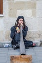 Street musician with long hair and a beard plays long pipe music leaning back against the wall of the house, sitting on the paveme Royalty Free Stock Photo