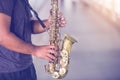 A street musician plays the saxophone with blurry people