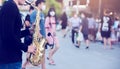 A street musician plays the saxophone and wearing face shield with blurry many people wearing mask and walking in Bangkok,