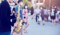 A street musician plays the saxophone and wearing face shield with blurry many people wearing mask and walking in Bangkok,