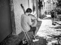 Street musician plays stringed instrument on Montmartre sidewalk with strolling couple in middle distance, Paris, late summer