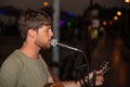 Street musician sings a song and plays the guitar in the evening. Concentrated singer performing, he is using a microphone Royalty Free Stock Photo