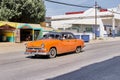 Street in non-tourist area of Havana,Cuba. Orange retro car taxi driving along road.