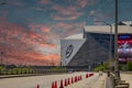 A street with orange cones and cars driving surrounded by Mercedes-Benz Stadium, lush green trees with powerful clouds at sunset