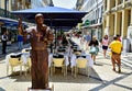 A street performer depicts a bronze figure of a statue of a monk with a little girl in her arms
