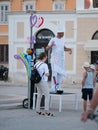 Street performer in white suit and fabulous hat makes inflatable toys out of long latex rubber balloons. Performance for children