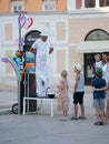 Street performer in white suit and fabulous hat makes inflatable toys out of long latex rubber balloons. Performance for children