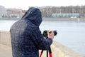 Street photographer in the process of shooting city landscapes. A camera on a tripod. A photographer in a jacket with a hood. Royalty Free Stock Photo