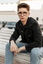 Street portrait american young hipster man with vintage glasses in fashionable denim wear in city at sunset. Handsome modern guy Royalty Free Stock Photo