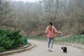 Street portrait of the back of a stylish woman on a walk with a puppy on a leash on an alley on a winter day in the park. Royalty Free Stock Photo