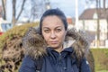 Street portrait of a beautiful dark-haired woman 40-45 years old in a jacket with a fur hood on a blurry urban background. Royalty Free Stock Photo