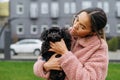 Street portrait of a cute girl with a black little dog in her hands, woman wearing a pink jacket, looking at a pet and smiling. Royalty Free Stock Photo