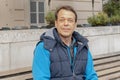 Street portrait of an elderly man 45-50 years old, sitting on a bench against a blurry urban background. Royalty Free Stock Photo