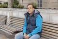 Street portrait of an elderly man 45-50 years old, sitting on a bench against a blurry urban background. Royalty Free Stock Photo