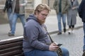 Street portrait of a fat young man with glasses and a beard 25-30 years old with blond hair, looking at a mobile phone against the