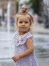 Street portrait of a little blonde girl against the background of city fountains. Her long hair is tied in a ponytail over her hea