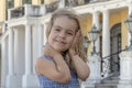 Street portrait of a little girl blonde, holding her hair back from the wind, smiling and looking at the camera. Royalty Free Stock Photo