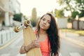 Street portrait of a mulatto girl holding a longboard in her hands, looking in camera, walking with a board in the evening. Girl