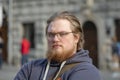 Street portrait of a serious, fair-haired 25-30-year-old man with glasses and a beard against the background of city buildings and Royalty Free Stock Photo