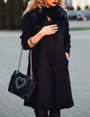 Street portrait shot of a beautiful young woman,dressed in black coat, on the shoulder fashion female bag, bracelets Royalty Free Stock Photo