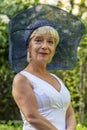 Street portrait of stylish and beautiful blonde woman 60-65 years old in a fashionable hat on the background of nature. Royalty Free Stock Photo